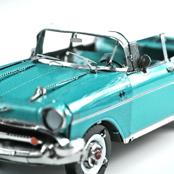 Een close-up van het 1957 Chevy metalen bouwpakket van SlimSpul nederland b.v. toont ingewikkelde details zoals de voorruit, koplampen, motorkap en zijspiegel van dit vintage cabrioletmodel tegen een witte achtergrond.