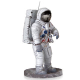 Het SlimSpul Apollo 11 astronaut - metalen bouwpakket heeft een wit ruimtepak met blauwe en rode accenten, een grote rugzak, donker reflecterend vizier en staat op een ronde grijze voet.