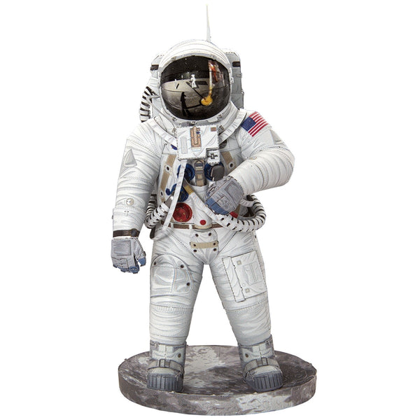 Een figuur van een Apollo 11 astronaut in een wit pak met een reflecterende helm staat op een grijze basis. Het is geïnspireerd op het SlimSpul "Apollo 11 astronaut - metalen bouwpakket" en heeft een patch met de Amerikaanse vlag en gedetailleerde uitrusting en slangen.