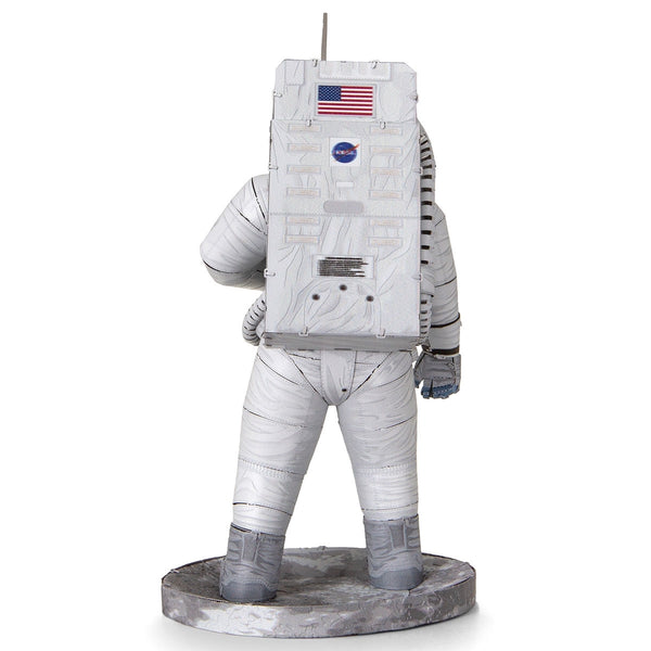 Een Apollo 11 astronaut in een wit pak staat op een grijs, rotsachtig oppervlak met een NASA-logo rugzak-ideaal als inspiratie voor jouw SlimSpul Apollo 11 astronaut - metalen bouwpakket model.
