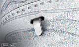 Close-up van een witte sneaker met textuur en een metalen veterhaak, geïnspireerd op de SlimSpul Apollo 11 astronaut - metalen bouwpakket. Gedeeltelijk in een gleuf gestoken; "Bend - Twist" staat in de linkerbenedenhoek.