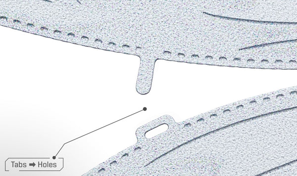 Close-up van twee gestructureerde, gebogen metalen stukken uit het SlimSpul Apollo 11 astronaut metalen bouwpakket, een met een lipje en de ander met een bijpassende gleuf. Een lijn met het label Tabs → Gaten laat zien hoe het maanlandingmodel in elkaar gezet moet worden.
