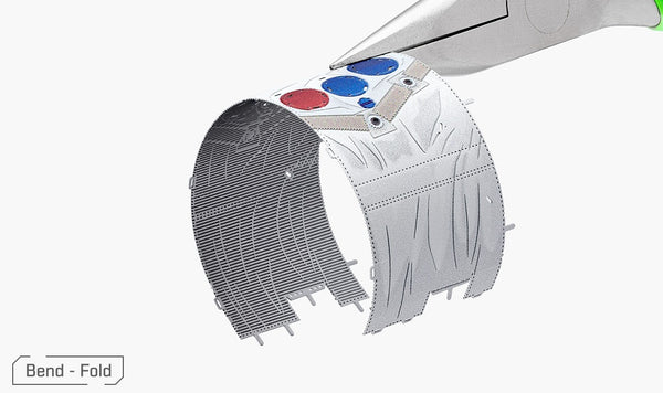 Een tang buigt een dunne plaat met ingewikkelde patronen uit het SlimSpul Apollo 11 astronaut metalen bouwpakket. Gekleurde cirkels versieren het metaal, terwijl een "Buig - Vouw" label linksonder verschijnt.