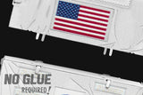 Close-up van twee witte, gestructureerde panelen met opgenaaide patches met de Amerikaanse vlag - ideaal voor je SlimSpul Apollo 11 astronaut - metalen bouwpakket. "NO GLUE REQUIRED!" staat vetgedrukt in de hoek op een zwarte achtergrond.
