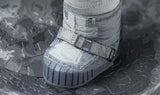 Een close-up van de laars van een Apollo 11-astronaut op het stoffige maanoppervlak is de inspiratiebron voor het Apollo 11 astronaut - metalen bouwpakket van SlimSpul, compleet met gedetailleerde riemen en treden op grijs, rotsachtig terrein.