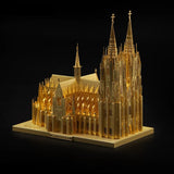 De Kathedraal van Keulen Metalen Bouwpakket van SlimSpul nederland b.v. is een gedetailleerd goud miniatuurmodel in Duitse gotische stijl met hoge torens en fijne details, afgebeeld tegen een zwarte achtergrond.