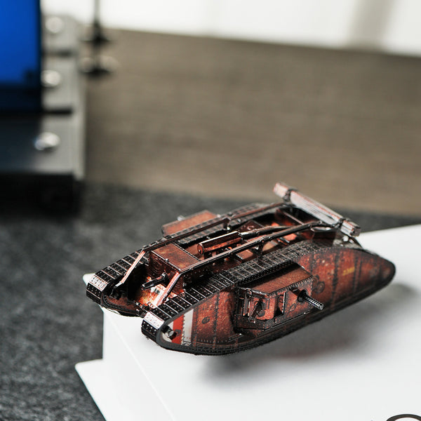 Het Mark IV tank metalen bouwpakket van SlimSpul nederland b.v. staat met zichtbare rupsbanden en metallic afwerking op een witte ondergrond, tegen een vervaagde achtergrond met lichte en donkere tinten.