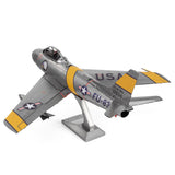Het F-86 Sabre metalen bouwpakket van SlimSpul nederland b.v. is een zilveren modelstraaljager met gele en zwarte details, USAF-embleem, staartnummer 12834 en FU-834 op de romp, geïnspireerd door de Koreaanse Oorlog. Wordt geleverd met standaard.
