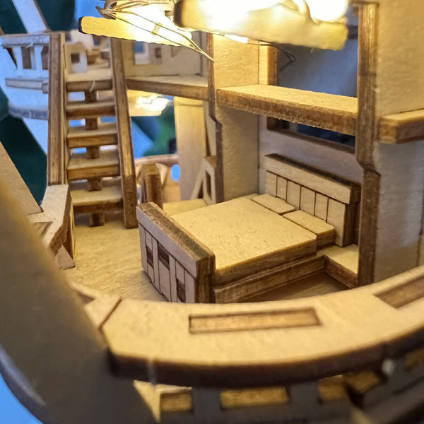 Close-up van het Horizons Edge DIY houten modelbouwpakket van Tiny Treehouses Europe, met een bed, trap en warme bovenverlichting met gedetailleerd vakmanschap en een gezellig interieurontwerp.