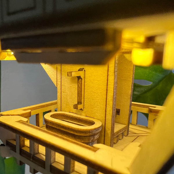 Een close-up van het Sky Lodge bouwpakket van Tiny Treehouses Europe laat een miniatuurbalkon zien met een bad, een reling en oplichtende LED-lampjes, die de gezellige charme van een boomtopverblijf oproepen.
