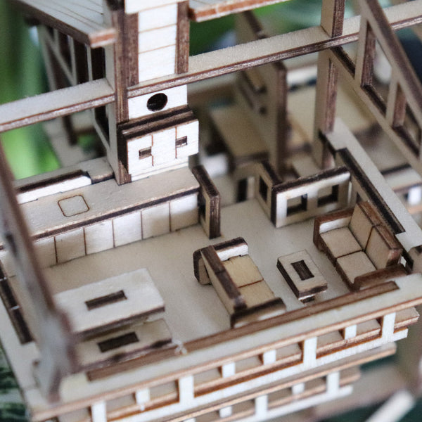 Close-up van het Tropical Lookout DIY houten modelbouwpakket van Tiny Treehouses Europe, met een modern interieur met meerdere verdiepingen, kamers, meubels en ingebouwde LED-verlichting. Inclusief een woonkamer met banken en een tafel.