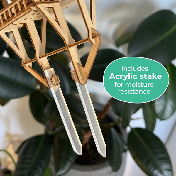 Close-up van de Tiny Treehouses Europe Tropical Lookout, een houten plantensteun met twee doorzichtige acryl palen voor vochtbestendigheid. Op het etiket staat: Inclusief acrylstokken. Perfect voor huizen in de jungle, groene bladeren op de achtergrond.