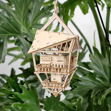 De Sky Lodge van Tiny Treehouses Europe is een klein, ambachtelijk houten bouwpakket van een huis met meerdere verdiepingen, balkons en een schuin dak, ontworpen om tussen weelderige groene bladeren te hangen.