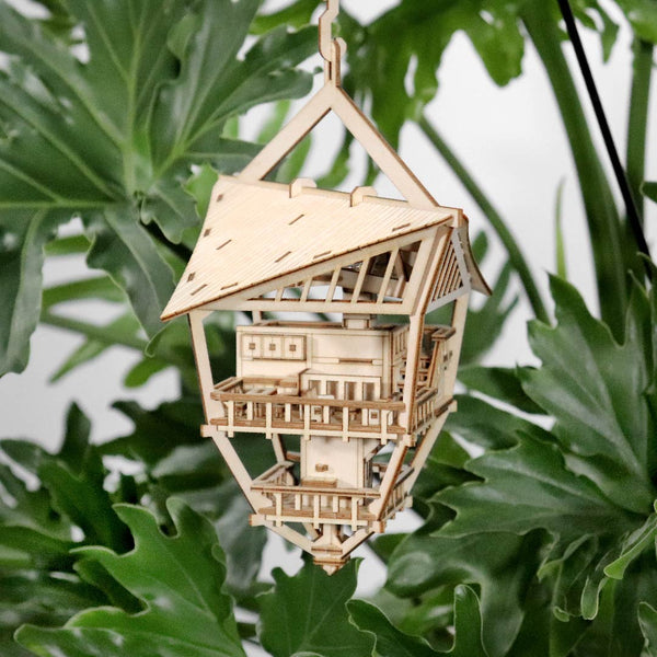 De Sky Lodge van Tiny Treehouses Europe is een klein, ambachtelijk houten bouwpakket van een huis met meerdere verdiepingen, balkons en een schuin dak, ontworpen om tussen weelderige groene bladeren te hangen.