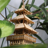 De Tempel van de Sereniteit DIY houten modelbouwpakket van Tiny Treehouses Europe is een kleine, meerlagige pagode met ingewikkelde rasterdetails en schuine daken, prachtig uitgestald tussen groene bladeren.