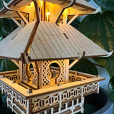 Een close-up van de Temple of Serenity DIY houten modelbouwpakket van Tiny Treehouses Europe, met ingewikkelde details en warme LED-verlichting tegen een achtergrond van groene bladplanten.