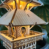Een close-up van de Temple of Serenity DIY houten modelbouwpakket van Tiny Treehouses Europe, met ingewikkelde details en warme LED-verlichting tegen een achtergrond van groene bladplanten.