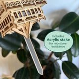 De Temple of Serenity van Tiny Treehouses Europe wordt getoond met een houten plantmarker en een acrylstaak, in de grond geplaatst naast een groenbladige plant. Een groen label vermeldt: Inclusief acrylstaak voor vochtbestendigheid.