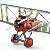 Close-up van een Sopwith Camel jachtvliegtuig metalen bouwpakket van SlimSpul nederland b.v.: rood-zilveren vintage dubbeldekker met tweebladspropeller, zichtbaar motorblok en vleugelsteunen tegen een witte achtergrond.