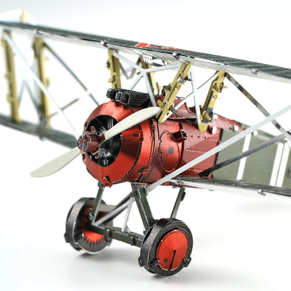 Close-up van een Sopwith Camel jachtvliegtuig metalen bouwpakket van SlimSpul nederland b.v.: rood-zilveren vintage dubbeldekker met tweebladspropeller, zichtbaar motorblok en vleugelsteunen tegen een witte achtergrond.