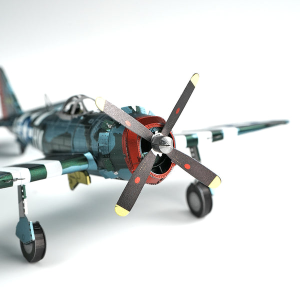Close-up van het P-47 Thunderbolt metalen bouwpakket van SlimSpul nederland b.v., een gedetailleerd WWII miniatuur jachtvliegtuig met camouflage verf en geel-getipte vierbladige propeller, weergegeven op een effen witte achtergrond.