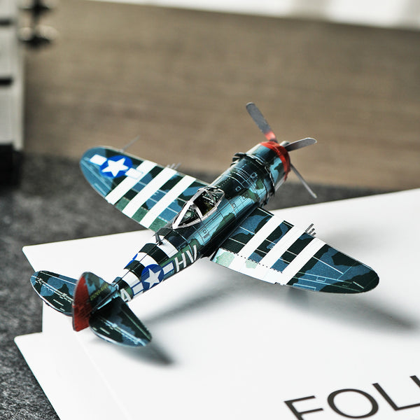 Het P-47 Thunderbolt metalen bouwpakket van SlimSpul nederland b.v. is een miniatuurmodel van het WOII-jachtvliegtuig met blauw-groene camouflage en witte strepen, prachtig gepresenteerd op een wit boek.