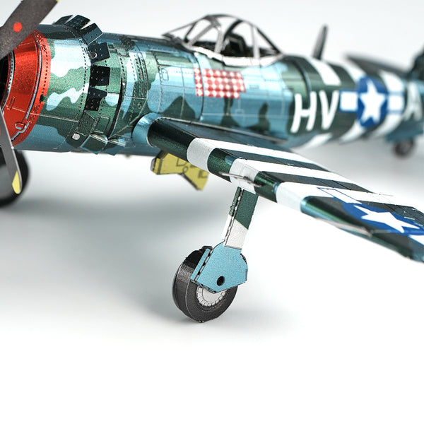 Close-up van het P-47 Thunderbolt metalen bouwpakket van SlimSpul nederland b.v., gedetailleerd met camouflageverf, witte vleugelstrepen, zichtbaar landingsgestel en een romp met blauw-witte ster insignes en "HV" letters.