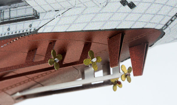 Close-up van het USS Midway vliegdekschip metalen bouwpakket van SlimSpul nederland b.v., met de nadruk op vier gouden propellers en roeren op een rode romp met een gedetailleerde witte bovenkant - een voorbeeld van dit iconische museumschip model.
