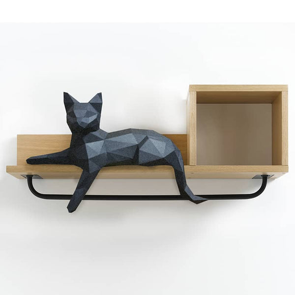 Zwarte kat met één hangend voorpootje als geometrisch papiermodel op een wandplank