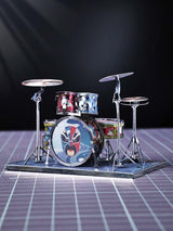 Het Drumstel Metalen Bouwpakket van SlimSpul nederland b.v. is een miniatuur muziekinstrument model met kleurrijk comic-artwork, inclusief basdrum, twee toms en twee bekkens op standaard, geplaatst op een paarse geruite ondergrond.