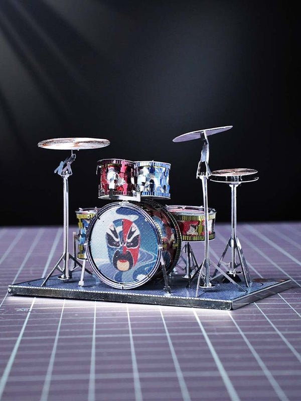 Het Drumstel Metalen Bouwpakket van SlimSpul nederland b.v. is een miniatuur muziekinstrument model met kleurrijk comic-artwork, inclusief basdrum, twee toms en twee bekkens op standaard, geplaatst op een paarse geruite ondergrond.