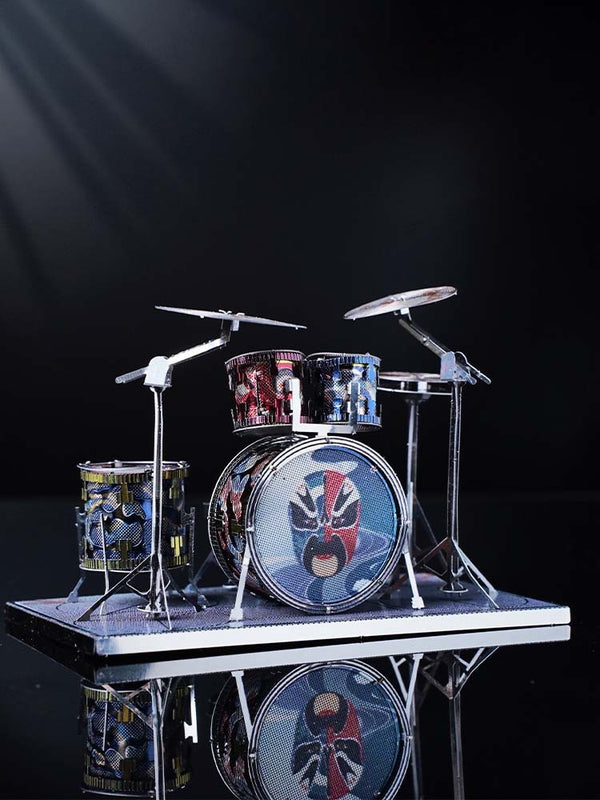 Het Drumstel Metalen Bouwpakket - Miniatuur Muziekinstrument Model van SlimSpul nederland b.v. heeft levendige drums met patronen op een klein platform, tegen een donkere, reflecterende achtergrond met zachte verlichting linksboven.