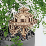 De Woodland Outpost van Tiny Treehouses Europe is een charmant zeshoekig doe-het-zelf houten modelbouwpakket, zittend op grijze kiezels in een plantenpot en omringd door delicate varenbladeren - perfect om speelsheid toe te voegen aan elke ruimte.