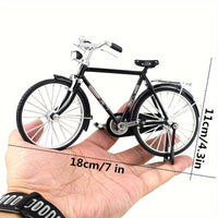 Iemand houdt het Stadsfiets Metalen Bouwpakket (1:8, Zwart of Groen) - Klassiek Fietsmodel van SlimSpul nederland b.v. vast; dit miniatuur is 18 cm lang en 11 cm hoog, met fijn gedetailleerde pedalen, stuur en spaken.