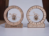Twee WoodTrick Kinetische Klok: Modern - Houten Klok Bouwpakket worden naast elkaar getoond. Op de linker staan tijdlabels, op de rechter dierenriemsymbolen. Beide klokken met zichtbare tandwielen hebben gedetailleerde uitgesneden ontwerpen van WoodTrick.