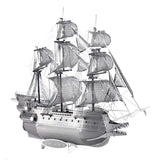 Het 3 masters, Queen Anne en Vliegende Hollander metalen bouwpakket van SlimSpul nederland b.v. is een gedetailleerd zilveren scheepsmodel met drie masten, zeilen en ingewikkelde ontwerpen, perfect voor scheepsmodellen fans. Weergegeven tegen een witte achtergrond.