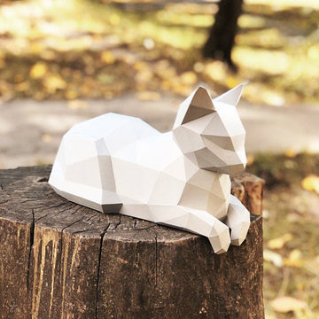 Witte liggende kat met pootjes voor als geometrisch 3D papiermodel op een boomstronk