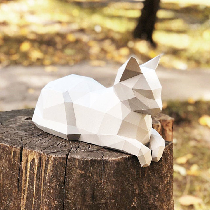Witte liggende kat met pootjes voor als geometrisch 3D papiermodel op een boomstronk