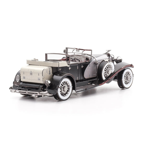 Een zwart met zilveren 1935 Duesenberg metalen bouwpakket klassieke oldtimer auto van SlimSpul nederland b.v. met beige kofferbak, spaakwielen en gedetailleerd dashboard, gezien van linksachter tegen een witte achtergrond.
