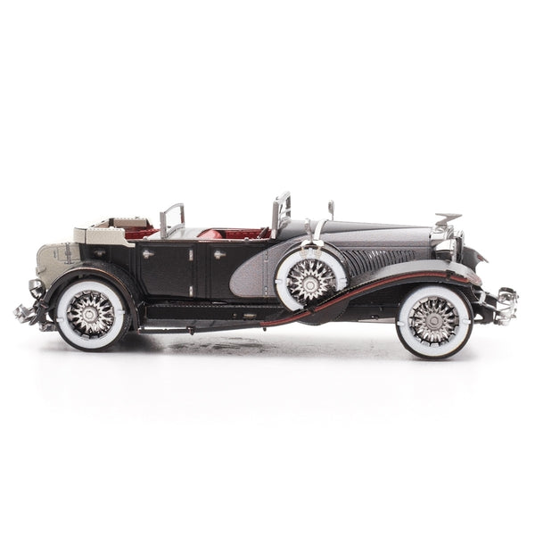 Het 1935 Duesenberg Metalen Bouwpakket van SlimSpul nederland b.v. is een gedetailleerde klassieke oldtimer modelauto in zwart en grijs, met whitewall banden, zijwielen en zichtbaar rood interieur, getoond in profiel op witte achtergrond.