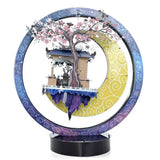 Het Jade Konijn in Maanpaleis Metalen Bouwpakket van SlimSpul nederland b.v. is een levendig cirkelvormig diorama met een prieel, een roze gebloemde boom en twee figuren eronder, tegen een blauw-gele ring met wervelpatroon geïnspireerd op de Chinese mythologie.