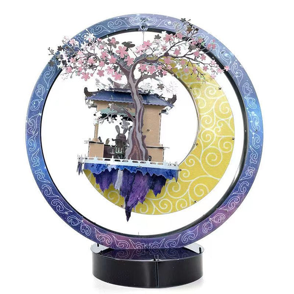 Het Jade Konijn in Maanpaleis Metalen Bouwpakket van SlimSpul nederland b.v. is een levendig cirkelvormig diorama met een prieel, een roze gebloemde boom en twee figuren eronder, tegen een blauw-gele ring met wervelpatroon geïnspireerd op de Chinese mythologie.
