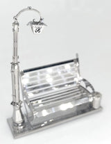 Het Parkbankje met Lantaarn Metalen Bouwpakket - Miniatuur Stadsgezicht van SlimSpul nederland b.v. heeft een gedetailleerde zilveren en glazen parkbank, straatlantaarn en afvalbak op een rechthoekige voet, perfect voor miniatuur stadsgezichten.