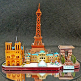Het Stadsgezichten Metalen Bouwpakket (Diverse Steden) - Architectuur Miniaturen van SlimSpul nederland b.v. toont een kleurrijk miniatuurmodel van Parijse iconen op een glanzende ondergrond: Eiffeltoren, Notre-Dame, Louvre en Arc de Triomphe.