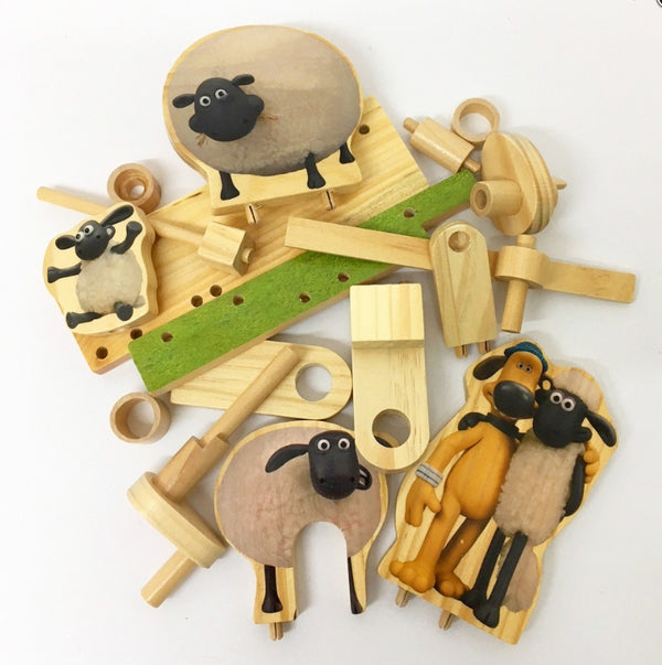 Aardman Jumping Timmy Houtconstructie - Beginner Model (Timberkits) van SlimSpul nederland b.v.: houten onderdelen en platte schapenfiguren met gaten, knijpers en accenten van groen vilt zijn verspreid over een wit oppervlak.