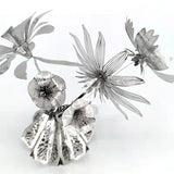 Een metalen sculptuur, die de elegantie van het SlimSpul nederland b.v. Vaasje met Bloemen Metalen Bouwpakket - Sierlijke Decoratie weerspiegelt, heeft gestileerde bloemen met geperforeerde bloemblaadjes en bladeren op een reflecterende basis tegen een witte achtergrond.