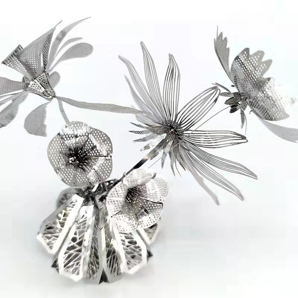 Een metalen sculptuur, die de elegantie van het SlimSpul nederland b.v. Vaasje met Bloemen Metalen Bouwpakket - Sierlijke Decoratie weerspiegelt, heeft gestileerde bloemen met geperforeerde bloemblaadjes en bladeren op een reflecterende basis tegen een witte achtergrond.