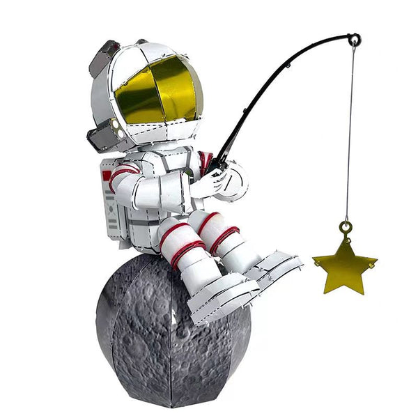 The Astronaut Vissend naar Sterren Metalen Bouwpakket van SlimSpul nederland b.v. toont een cartoon ruimtevaarder met goud vizier op de maan, vissend naar sterren-ideaal als decoratie of voor je volgende modelbouwproject!.