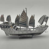 Het Schatschip van Zheng He Metalen Bouwpakket - Chinees Jonk Model van SlimSpul nederland b.v. is een gedetailleerd zilverkleurig bouwpakket met meerdere zeilen en decoratieve details, getoond op een grijze achtergrond.