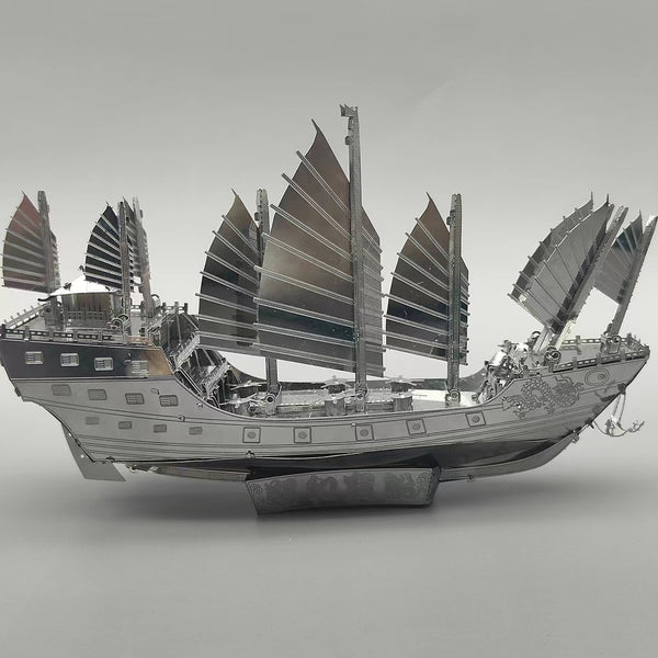 Het Schatschip van Zheng He Metalen Bouwpakket - Chinees Jonk Model van SlimSpul nederland b.v. is een gedetailleerd zilverkleurig bouwpakket met meerdere zeilen en decoratieve details, getoond op een grijze achtergrond.